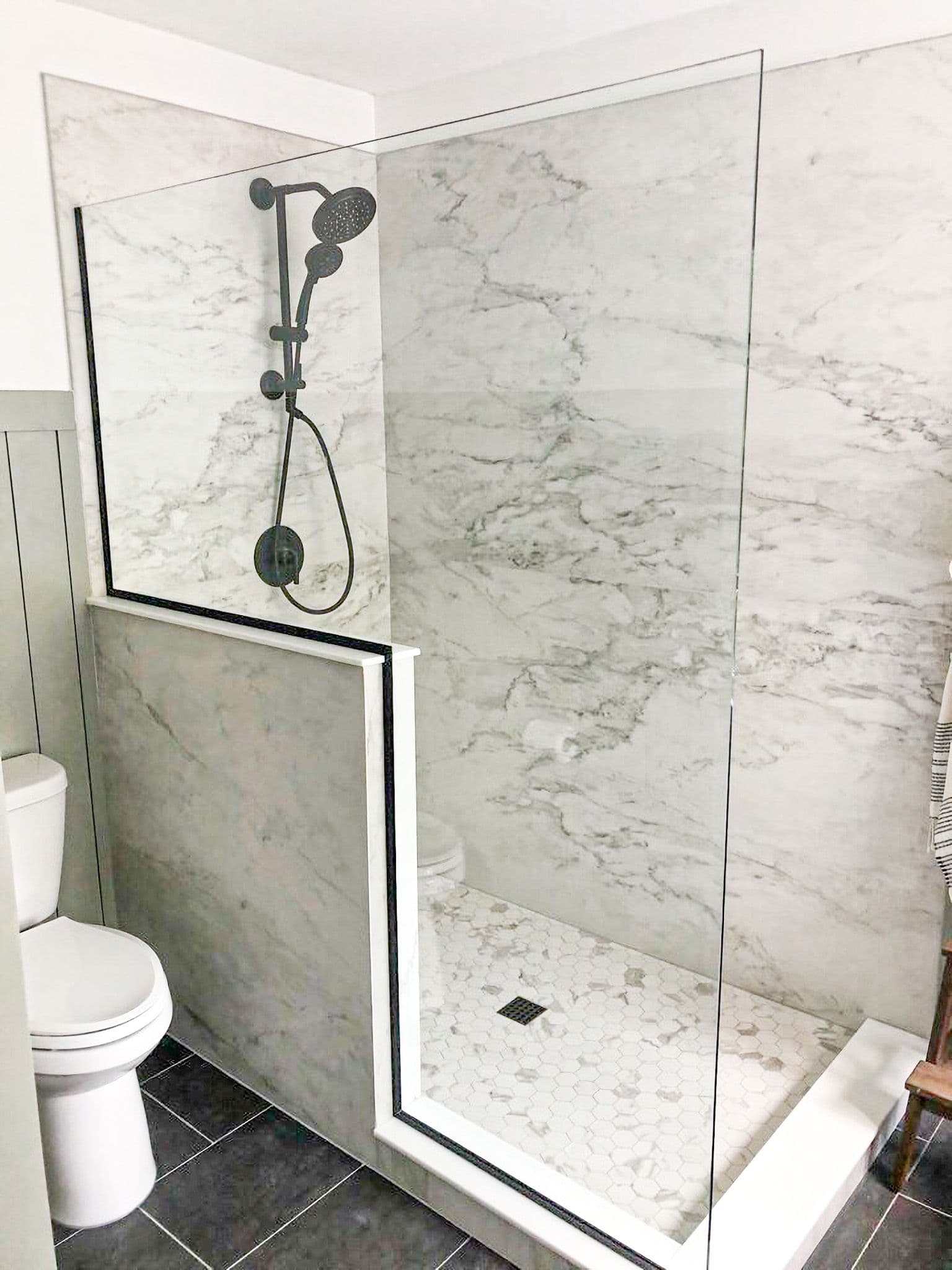 A walk-in shower with half wall and glass partition and white marbled walls.