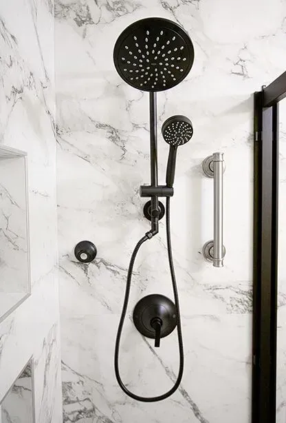 A matte black showerhead with handheld attachment in a shower with white and gray marbled walls.