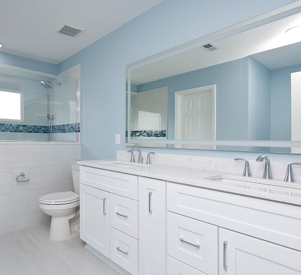 A blue bathroom with white cabinets, walk-in shower with a half-wall and glass partition, rectangular tile walls, and blue mosaic tile horizontal accent.