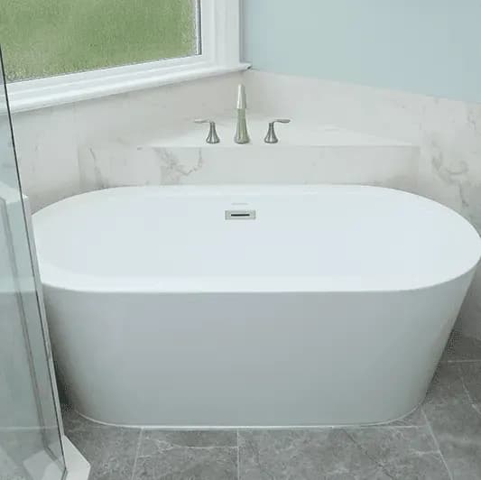 A white, oval-shaped, free-standing soaking bathtub in the corner of a bathroom.