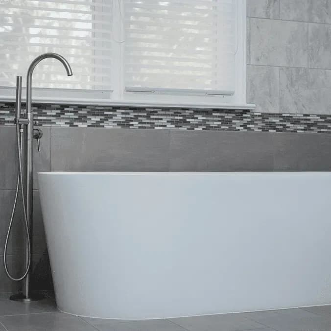 A free-standing custom bathtub with gray mosaic tile walls in the background.