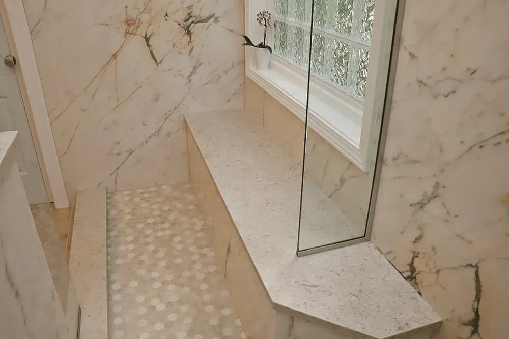 A walk-in shower with marbled walls, hexagonal tiled-floor, and built-in bench.