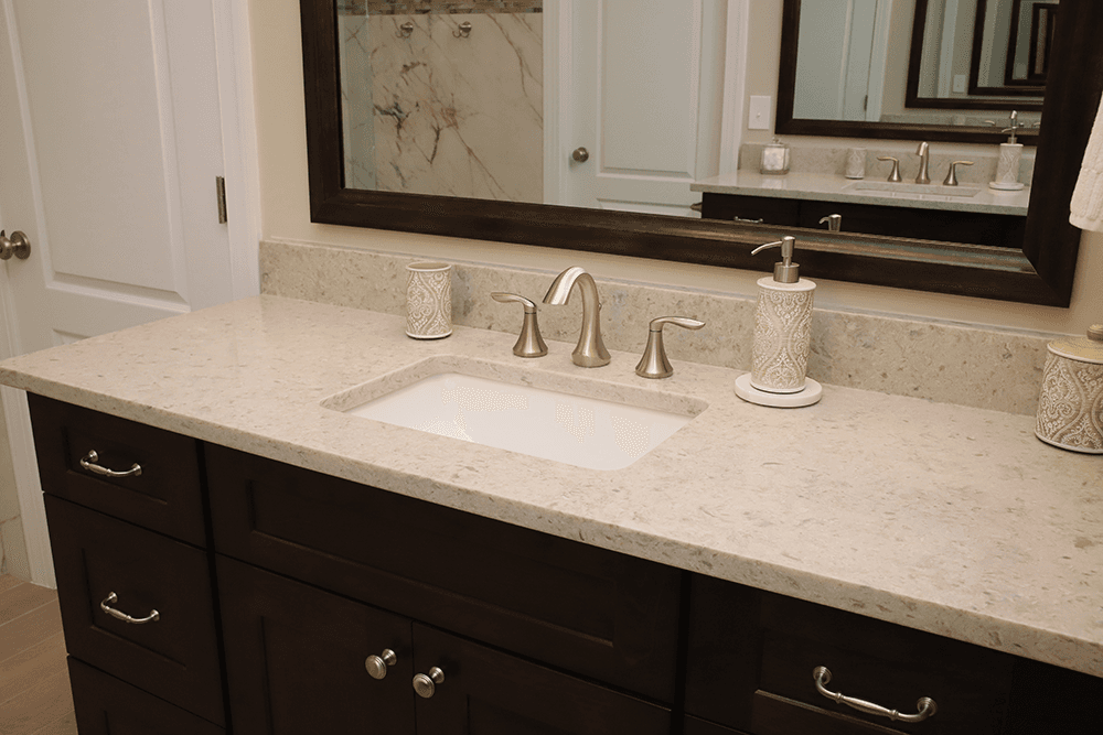 A bathroom sink with brushed metal faucet and fixtures, light-colored countertop, and dark brown cabinets.