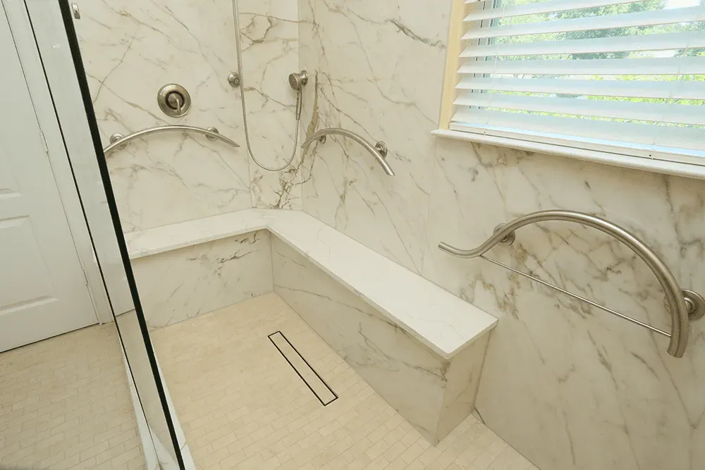 A walk-in shower with marbled walls, built-in stone bench, and multiple curved grab bars.