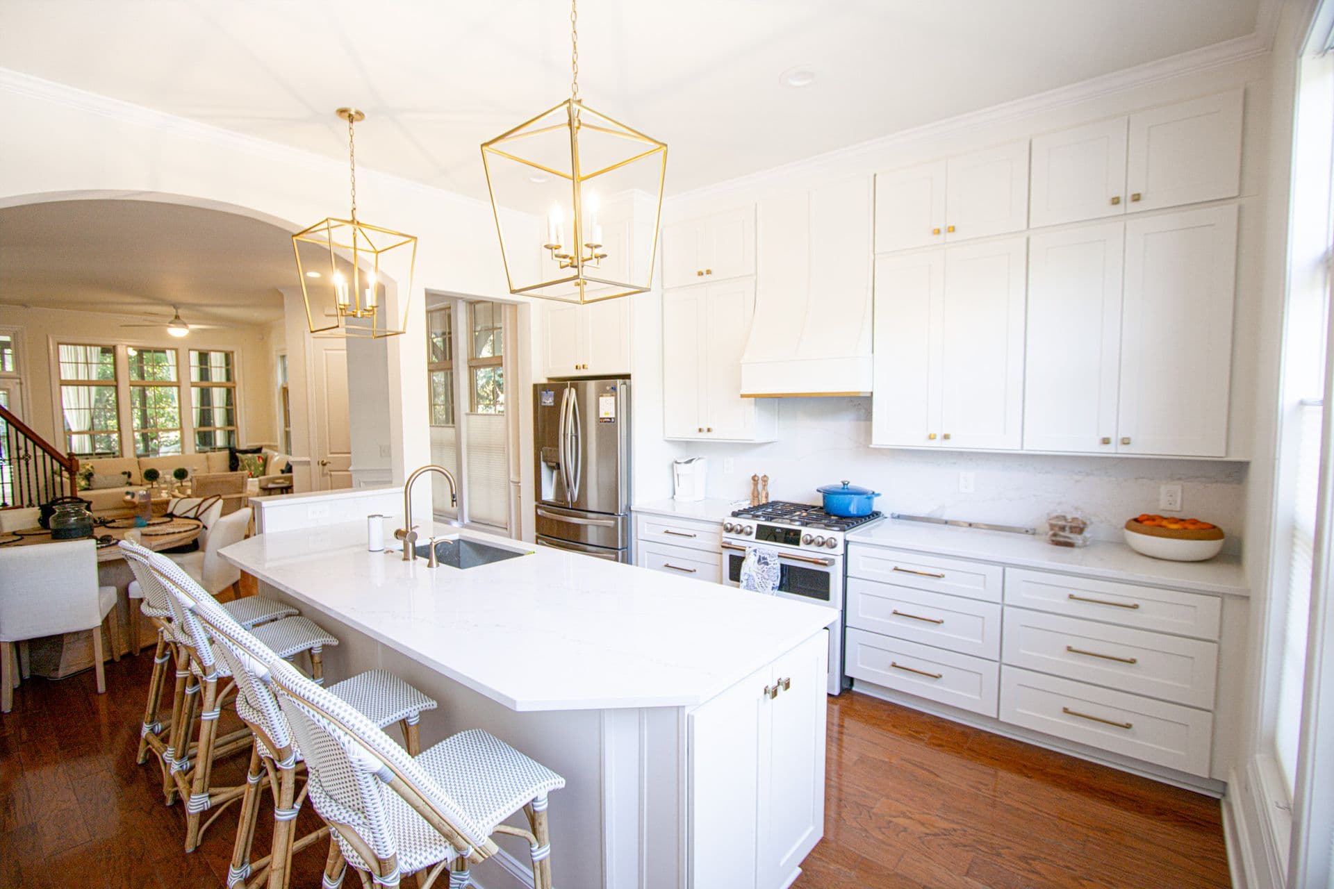 A white kitchen with white cabinets with gold fixtures, large central island with white countertop and bar stool seating, and hanging gold lamps.