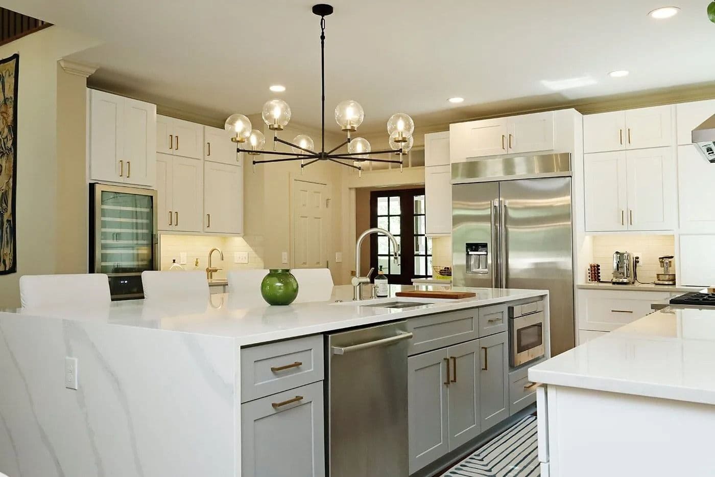 A kitchen with white cabinets, gold fixtures, white marbled countertops and large central island.