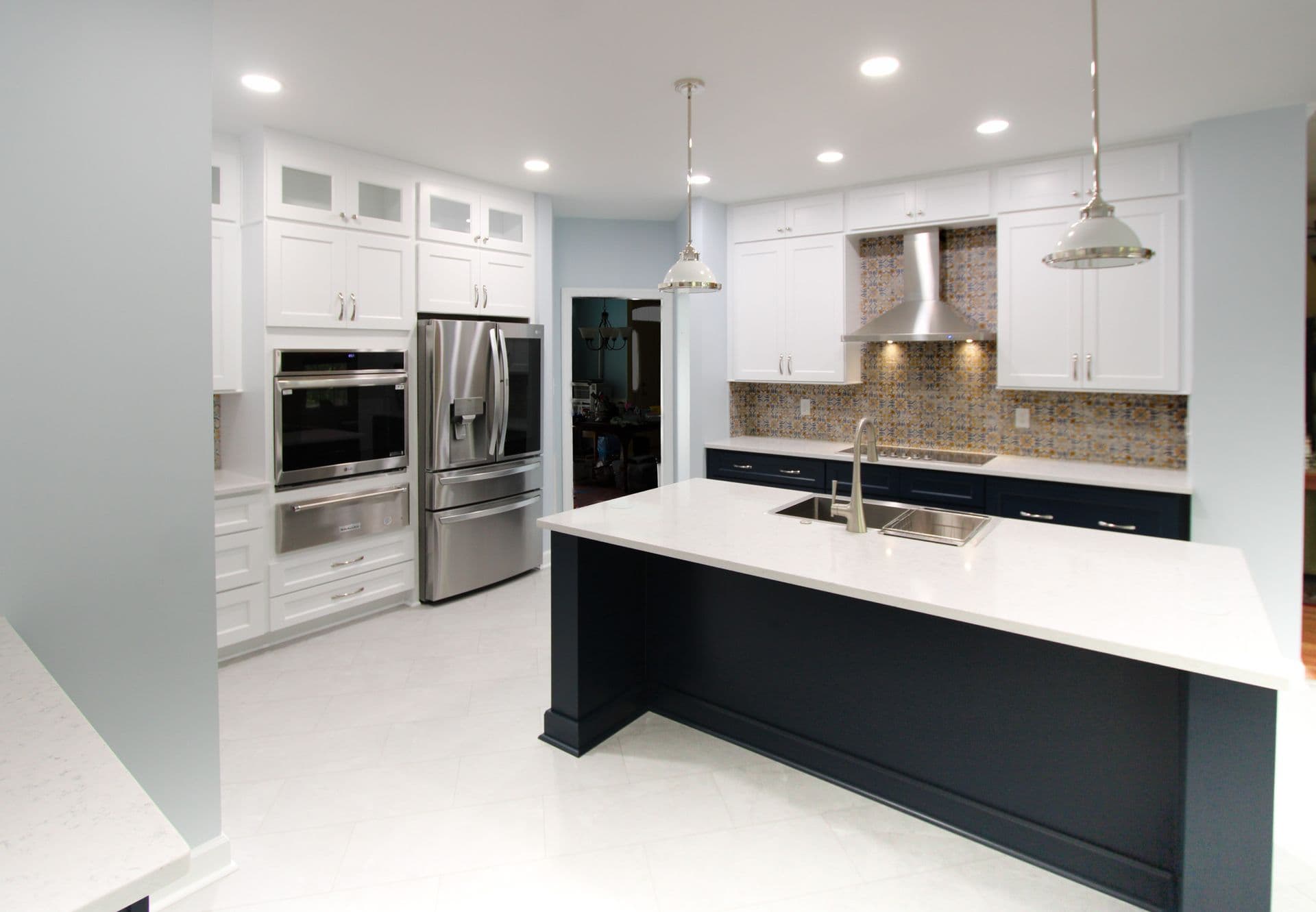 A kitchen with white cabinets, large central island with white countertop and black base, and a geometric tile backsplash.