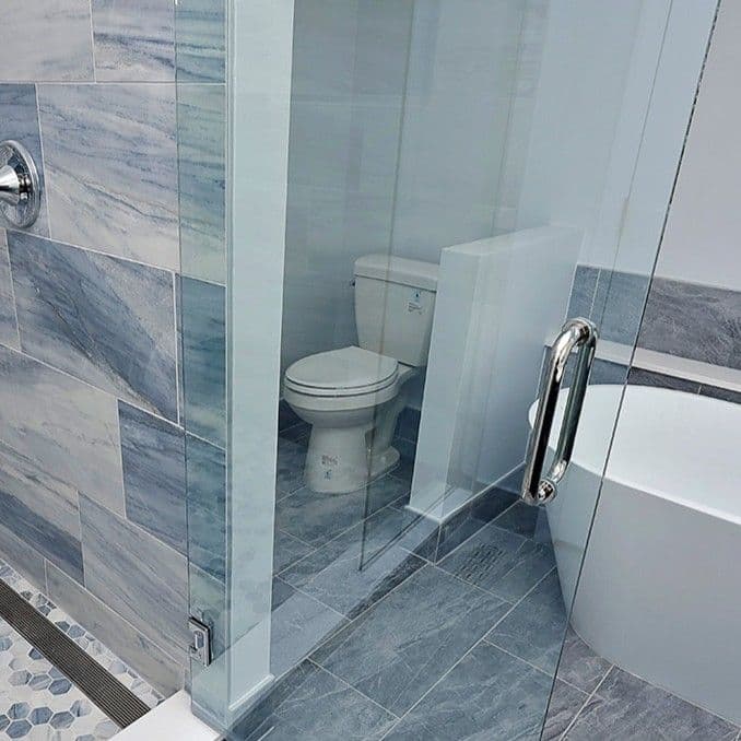 A toilet in a blue tiled bathroom. A walk-in shower is to the left, and a soaking tub is to the right.