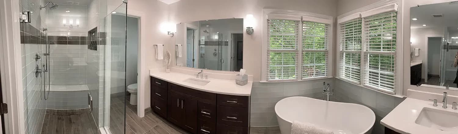 A panoramic view of a newly-remodeled bathroom with a walk-in shower and a large free-standing soaking bathtub.